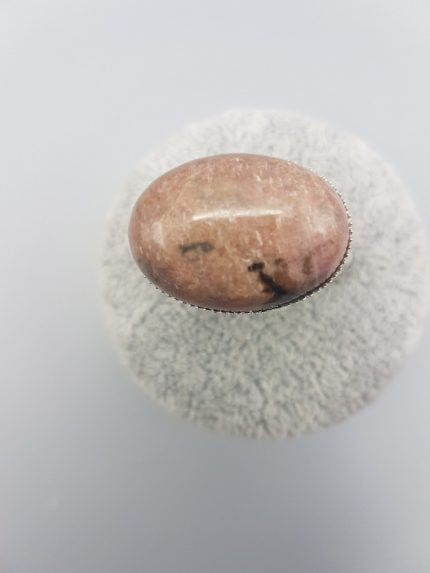 Un ANELLO DI RODONITE OVALE 25X18 rosa appoggiato su una superficie bianca.