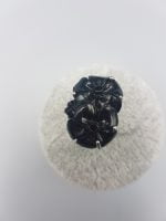 Un anello con fiore nero in resina su una superficie bianca.