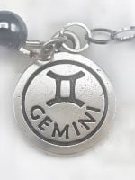 Una collana con sopra il nome del prodotto BRACCIALE DI EMATITE E HOWLITE CON CIONDOLO GEMELLI.
