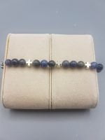 Un BRACCIALE DA UOMO CON SODALITE ELASTICO blu e argentato con una croce su di esso.