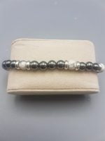 A BRACCIALE DI EMATITE E HOWLITE CON CIONDOLO GEMELLI con perline argento e bianche in una scatola.