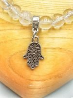 A 6 MM ROCK CRYSTAL BRACELET WITH HAND OF FATIMA PENDANT on wooden panel.