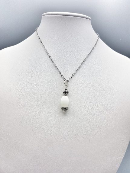 A WHITE AGATE BARREL PENDANT on a silver chain.