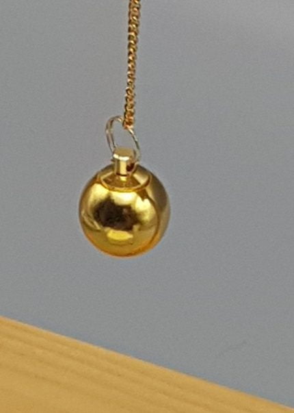 A SPHERICAL BRASS PENDULUM hanging from a chain.