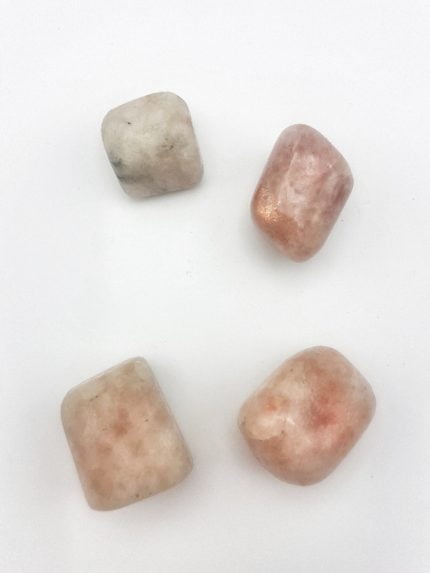 Three pieces of pink and white stones on a white surface, depicting TUMBLED SUNSTONE.