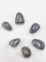 A group of black and grey tumbled LABRADORITE stones arranged on a white surface.