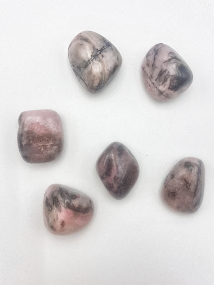 Gruppo di pietre rosa e nere su fondo bianco con Rodonite Burattata.