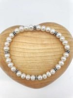 A white PEARL BRACELET on a wooden heart.