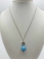 Una collana con una pietra blu e una catena d'argento, caratterizzata da un CIONDOLO SFERICO IN ANGELITE.