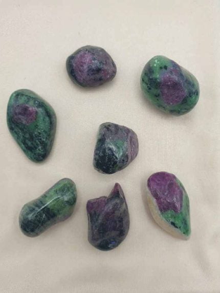 Un grappolo di pietre Zoisite verdi e pietre Rubino Burattata viola disposte su un panno bianco. [ZOISITE RUBINO BURATTATA]