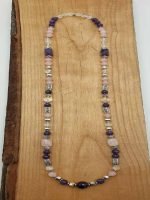 LA COLLANA AMETISTA, QUARZO ROSA E CRISTALLO DI ROCCA. con perle di Quarzo Rosa e Cristallo di Rocca esposte su una tavola di legno.