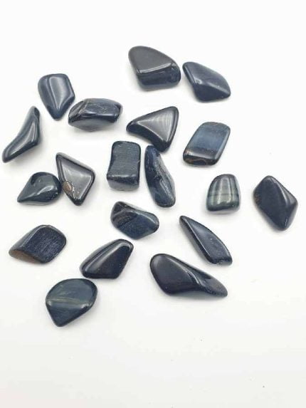 A group of black stones on a white surface, TUMBLED HAWK'S EYE.