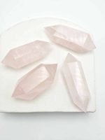 Four BITERMINATED ROSE QUARTZ TIPS on a white surface.