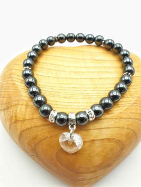 A HEMATITE BRACELET WITH TRANSPARENT SWAROVSKI HEART AND RHINESTONES with heart charm.
