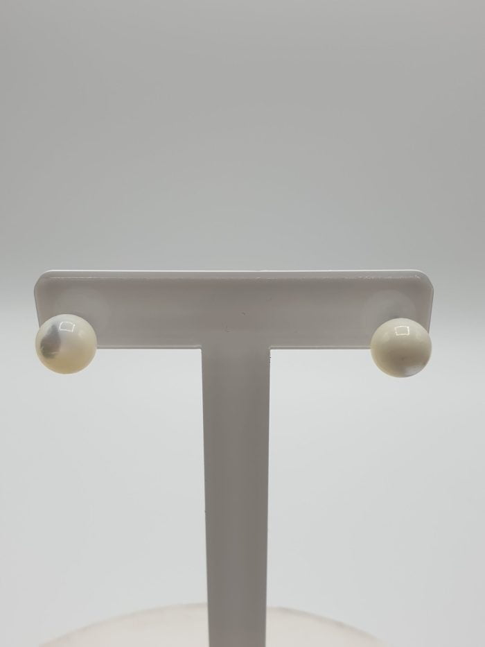 Pair of white stud earrings on a stand made of mother-of-pearl and silver.