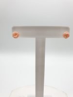 A pair of PINK CORAL EARRINGS IN THE SHAPE OF A SILVER FLOWER on a white stand.
