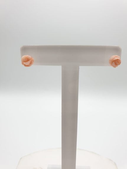 A pair of PINK CORAL EARRINGS IN THE SHAPE OF A SILVER FLOWER on a white stand.