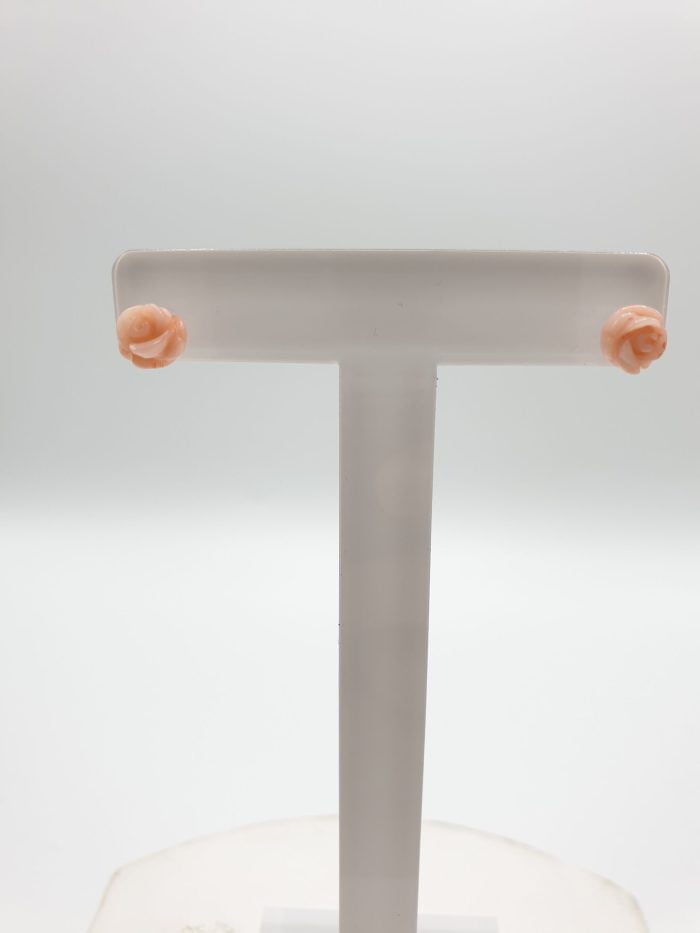 A pair of PINK CORAL EARRINGS IN THE SHAPE OF A SILVER FLOWER on a white stand.