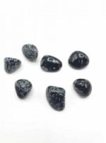 A group of black and white stones on a white surface that intricately resembles Obsidian Tumbled Snowflakes, also known as snowflakes, with a tumbled twist.