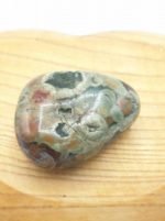 A piece of green and brown TUMBLED RHYOLITE on a wooden board.