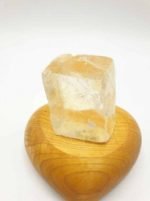 A piece of quartz on top of a wooden heart with CUBES OF GOLDEN CALCITE.