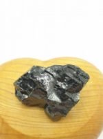 Una PIETRA PEPITE SHUNGITE ELITE GREZZA seduta sopra un cuore di legno.