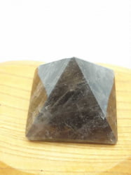 UNA PIRAMIDE DI QUARZO FUME' CM 3 in quarzo nero, posta su un tavolo di legno.