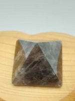 A SMOKY QUARTZ PYRAMID 3 CM ABOVE a wooden table.