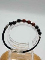 A BRACCIALE DA UOMO CON ONICE NERO, DIASPRO ROSSO E CORDINO CUOIO NERO con perline rosse e nere su supporto in legno e cordino in cuoio.