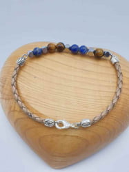 A BRACCIALE UOMO CON SODALITE, OCCHIO DI TIGRE E CORDINO CUOIO MARRONE CHIARO caratterizzato da perline blu e un cuore con accenti argento.