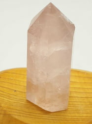 A rose quartz obelisk tip on top of a wooden table.