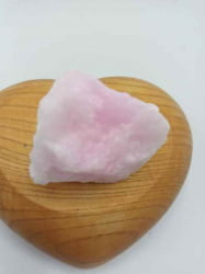 Una pietra ARAGONITE ROSA GREZZA appoggiata su un cuore di legno.