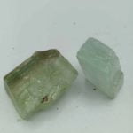 Due pezzi di calcite verde grezza naturale su una superficie bianca.