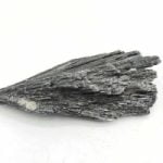 A natural raw black kyanite on a white surface.