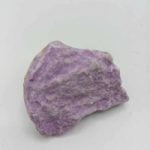 Un pezzo grezzo di Fosfosiderite Grezza Naturale viola su una superficie bianca.