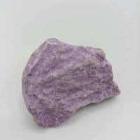 Un pezzo grezzo di Fosfosiderite Grezza Naturale viola su una superficie bianca.