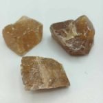 Tre pezzi di quarzo CALCITE MIELE O DORATA GREZZA NATURALE marrone su superficie bianca.