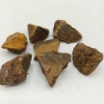 A group of pieces of NATURAL RAW GOLDEN TIGER'S EYE wood on a white surface, showing a raw natural aesthetic.