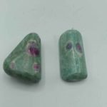 Due cabochon RUBINO FUCHSITE BURATTATO su superficie bianca.