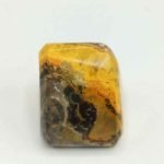 A piece of yellow and black BUMBLEBEE TUMBLED JASPER agate on a white surface.