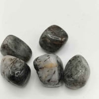 A collection of TUMBLED TOURMALINATED QUARTZ stones on a white surface.