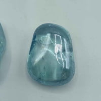 Two Aqua Aura Azzurra Tumbled Quality A stones on a clear surface.